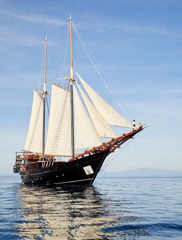 Traditional sailing yacht Amandira with cream canvas sails on calm blue waters.