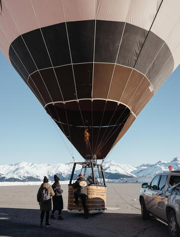 Hot air balloon tethered on the ground at Aman Le Mélézin, with passengers preparing for flight in the French Alps.