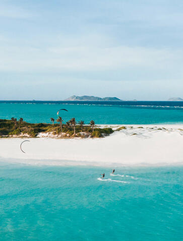 Kitesurfer on turquoise waters at Amanpulo, Philippines, with white sand beach and distant islands.