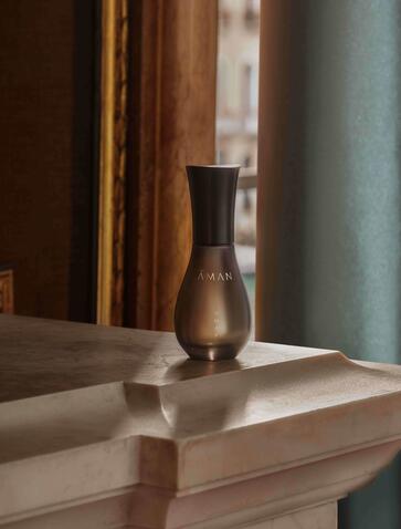 Aman Venice fragrance bottle displayed on a white surface with wooden and pale blue architectural details.