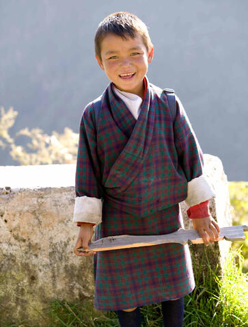 Young boy in traditional Bhutanese dress standing by a roadside at Amankora, smiling at the camera.