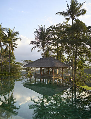 Amandari's swimming pool reflecting surrounding palms and pavilion at dusk, Bali.