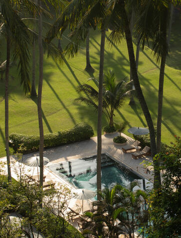 Overhead view of Amankila's beach club framed by swaying palm fronds, with sun loungers and pool below.