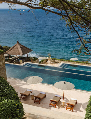Amankila's main pool overlooking the Indian Ocean, with sun loungers and umbrellas on the terrace below.