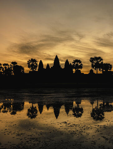 Angkor Wat temple silhouetted against golden dawn sky, reflected in still water at Amansara.