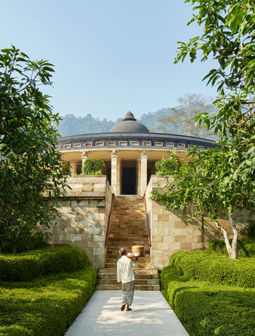 Walkway leading to a stone pavilion at Amankila, framed by green foliage and mountain views beyond.