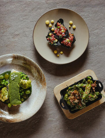 Three dining plates at Amangani featuring roasted vegetables and garnishes on stone surface.