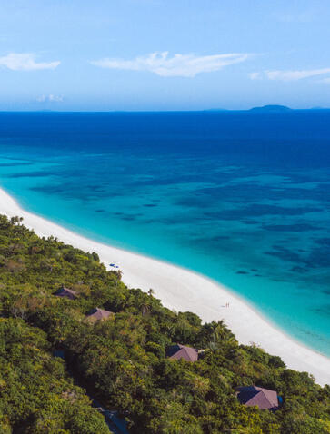 Aerial view of Pamalican Island showing white sand beach, turquoise waters and forested coastline at Amanpulo resort.