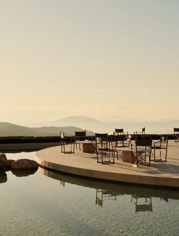 Exterior bar at Amanzoe with wooden deck overlooking still waters at dusk, Greece.