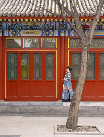 Gnarled tree trunk stands before a red-walled pavilion with ornate roof at Aman Summer Palace, China.