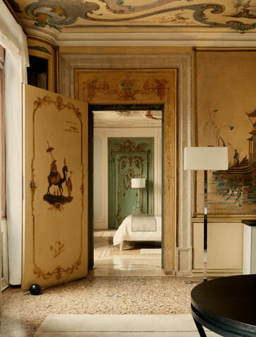 Alcova Tiepolo Suite living room at Aman Venice, with gilt-framed doorways and warm ochre walls.
