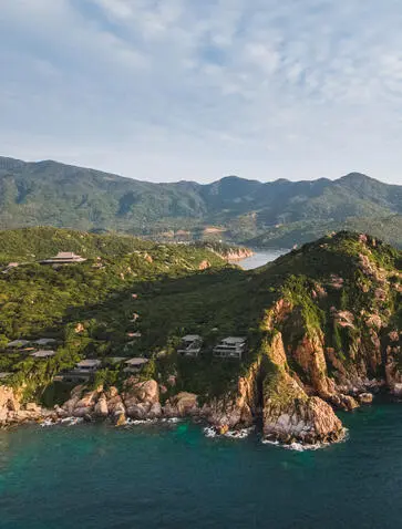 Amanoi accommodation perched on a clifftop overlooking turquoise waters and forested mountains in Vietnam.