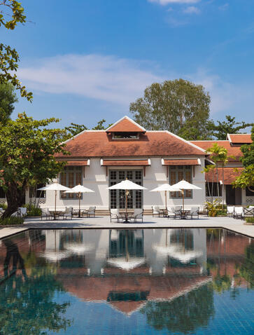 Amantaka's ochre-roofed pavilion reflected in still pool waters, surrounded by tropical greenery.