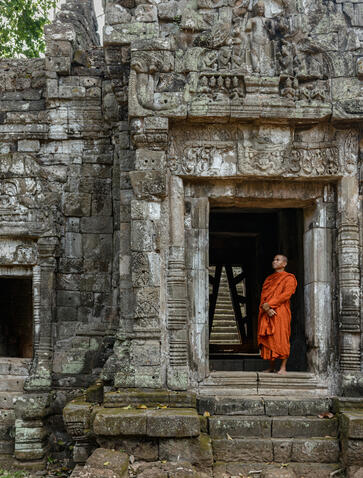 Buddhist monk in saffron robes standing in doorway of ancient stone temple at Amansara, Cambodia.