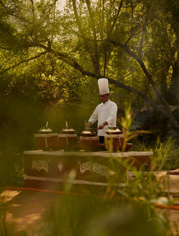 A chef prepares a meal at a wooden table set amongst jungle foliage at Aman-i-Khas.