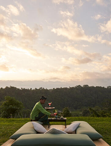 Two guests enjoying sundowner cocktails on a cushioned daybed overlooking rice terraces at Amandari, Bali.