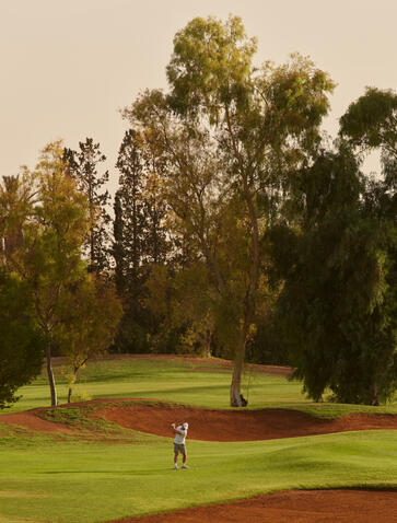 Terrain de golf du resort Amanjena au Maroc, avec joueurs sur le parcours verdoyant.