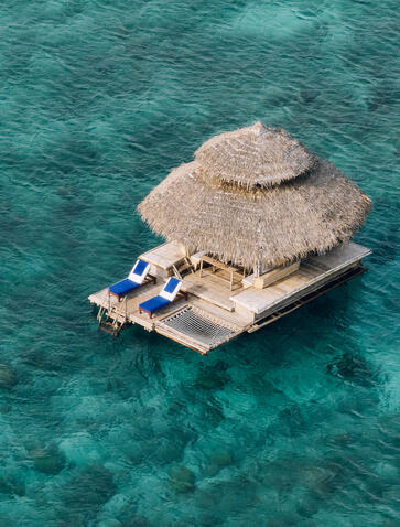 Aerial view of the floating Kawayan Bar at Amanpulo, Philippines, with thatched roof structure on turquoise water.