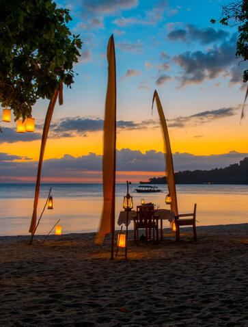 Candlelit dinner table on beach at sunset, Amanwana.