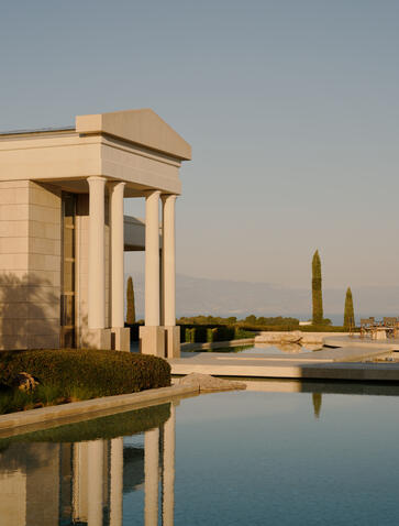 Amanzoe resort, Porto Heli: Classical stone pavilion reflected in still water at dusk, with distant monument.