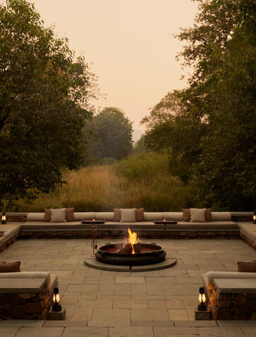 Outdoor firepit at Aman-i-Khas with stone seating and tree-lined vista at dusk.