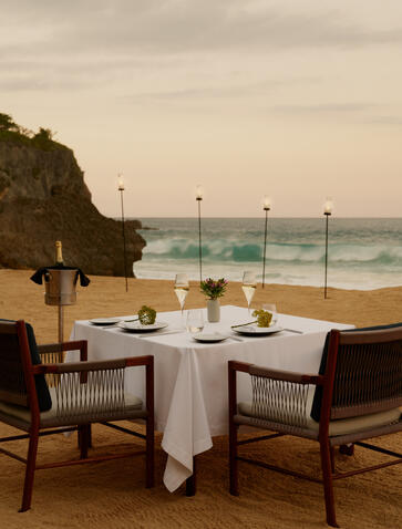 Candlelit dining table for two overlooking the Dominican coastline at Amanera, with waves and cliffs visible beyond.