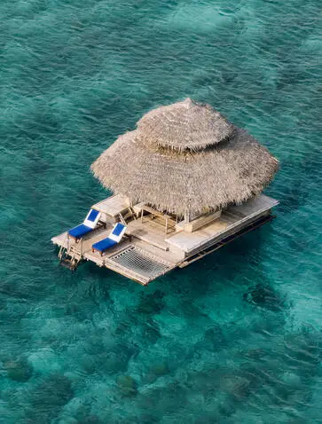 Aerial view of Kawayan Bar at Amanpulo, a thatched-roof structure floating on turquoise Philippine waters.