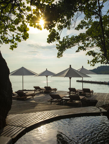Shaded beach deck at Amanwana with umbrellas and loungers overlooking calm waters at sunrise, Sumbawa, Indonesia.
