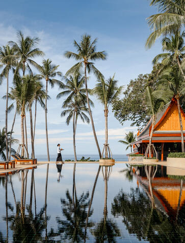 Ben Richards photograph of a serene pool reflecting palm trees and traditional Thai architecture at Amanpuri resort.