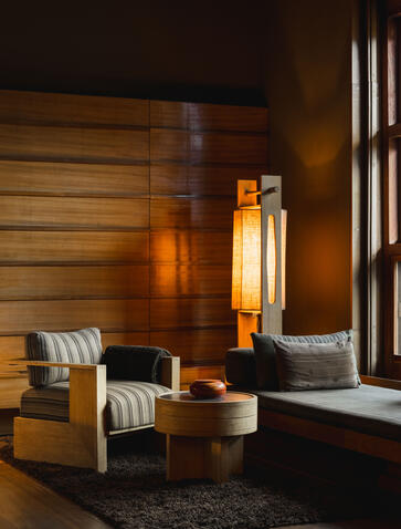 Gangtey Lodge suite interior with wooden walls, striped armchair, amber-toned lighting, and window overlooking Bhutan's Phobjikha Valley.