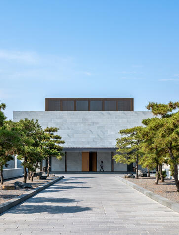 Amanyangyun lobby exterior with modernist white building, tree-lined courtyard and clear sky.