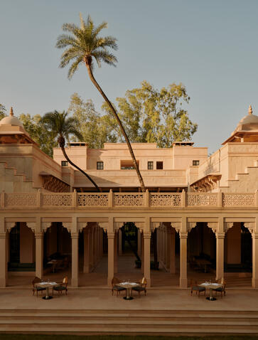 Amanbagh's main building exterior with a palm tree and courtyard framed by terracotta arches.