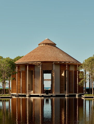 Main bar at Amanyara overlooks the ocean, with thatched roof and wooden structure reflected in still water.