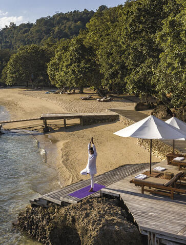 Guest practising yoga on wooden deck at Amanwana, Sumbawa, Indonesia, at sunrise.