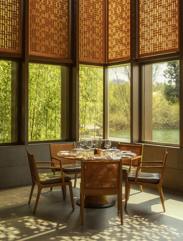 Circular dining table and chairs beside latticed windows overlooking gardens at Amanyangyun, China.