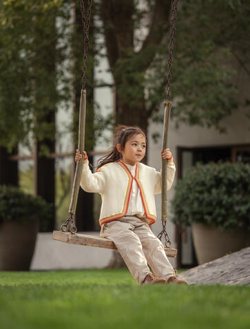 A woman sits peacefully on a bench among birch trees in the garden at Amanyangyun, wearing a cream linen shirt.