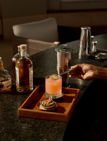 Bar setup at Amanyara resort with amber cocktail, bottles, and mixing tools on wooden tray.