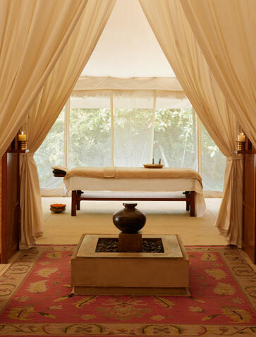 Spa treatment room at Aman-i-Khas with draped curtains, massage table, and window overlooking Indian landscape.