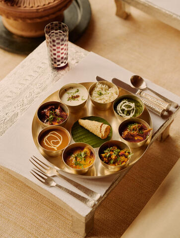 Overhead view of a traditional Gwaadi cooking class at Amanbagh, showing a circular wooden platter with various spices and ingredients arranged in small bowls.