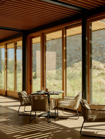 Sarika Restaurant at Amangiri resort, with floor-to-ceiling windows framing desert views and wooden chairs on striped flooring.