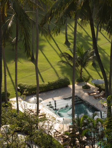 Coastal dining venue at Amankila resort framed by palm fronds, overlooking a sandy beach in Bali.