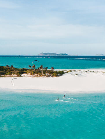 Kite surfer gliding across turquoise waters near a white sand island at Amanpulo resort, Philippines.