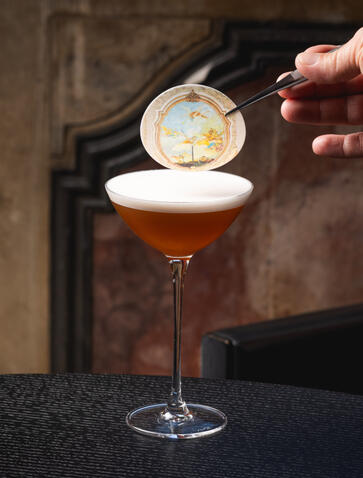 Bartender pouring foam into an amber cocktail at Aman Venice bar in Italy.