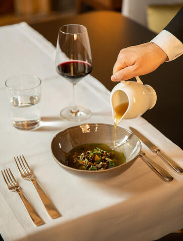Hand pouring sauce over a dish at Aman Venice restaurant table setting.