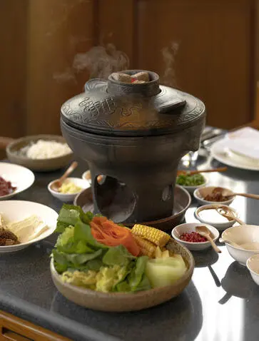 大研安缦度假村的黑陶火锅，热汤冒烟，周围摆放食材和餐具。