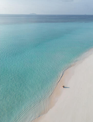 Aerial view of Amanpulo's white sand beach meeting turquoise waters with a solitary boat.