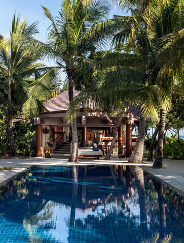 Amanpulo villa with infinity pool reflecting palm trees and sky, wooden structure nestled among tropical vegetation.