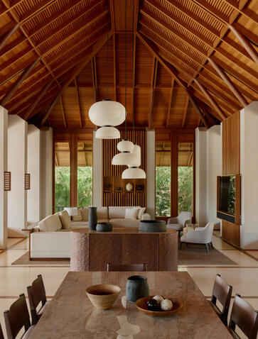 Amanyara villa interior with soaring wooden ceiling, cream furnishings, and floor-to-ceiling windows overlooking tropical landscape.