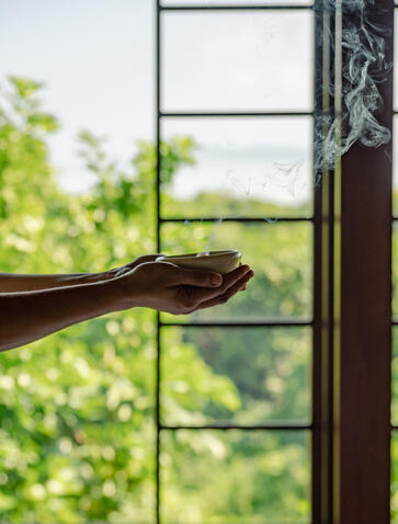 Hand resting on wooden window frame at Amanpulo, Philippines, with garden view beyond.