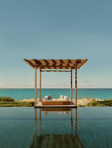 Wooden pergola with canopy beside a still pool overlooking turquoise sea at Amanyara, Turks and Caicos.